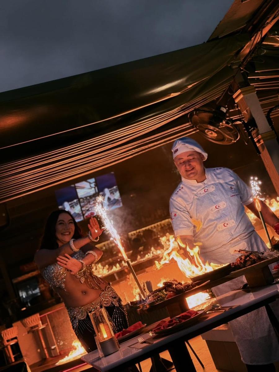 Chef cooking over open flames beside a belly dancer at Khubani Rooftop Bar in Patong